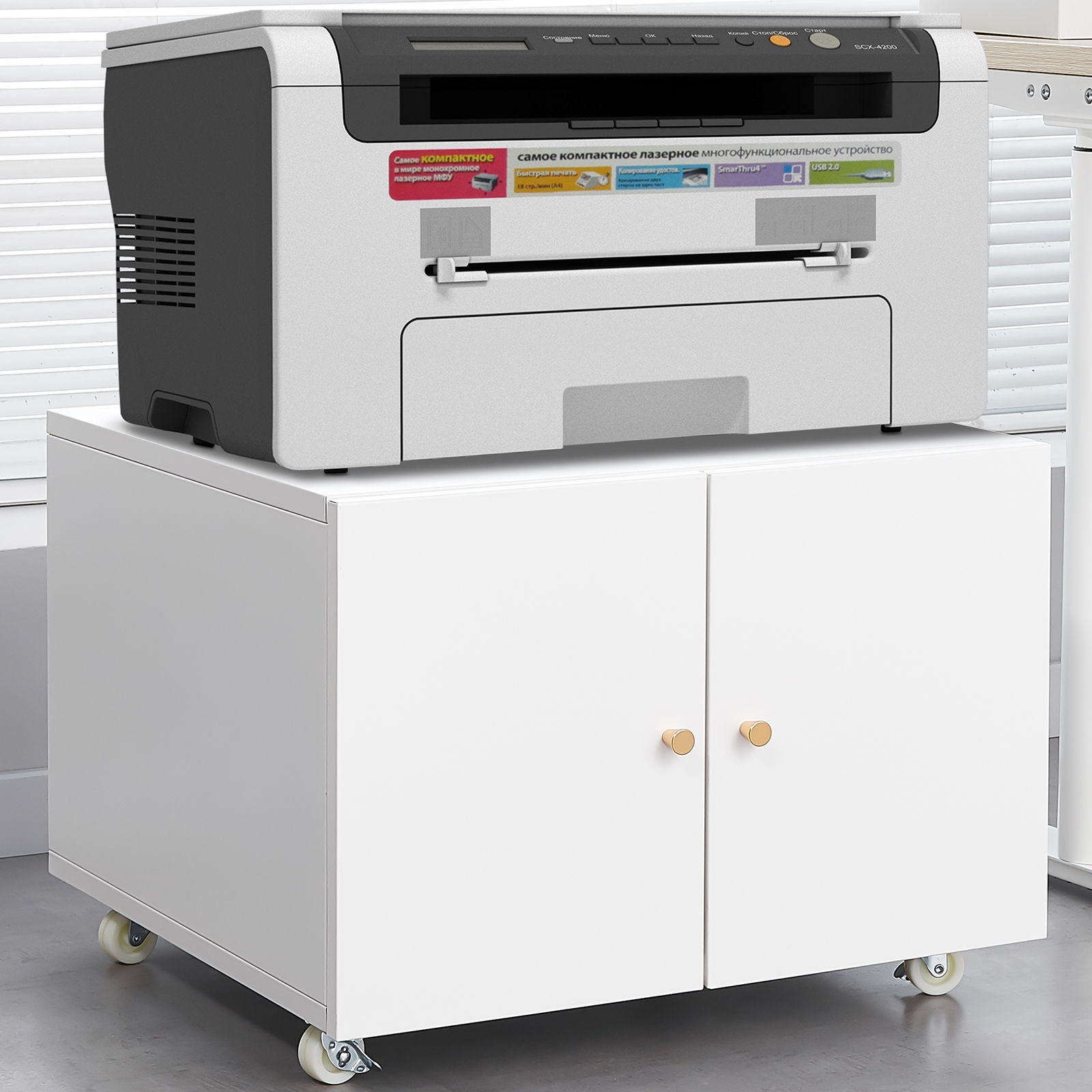 An Office Furniture Copier Cabinet 2 Door Steel Copier Stand Mobile Pedestal File Printer Stand with wooden knobs and wheels holds a black and gray printer, positioned on a gray floor near a window with blinds.