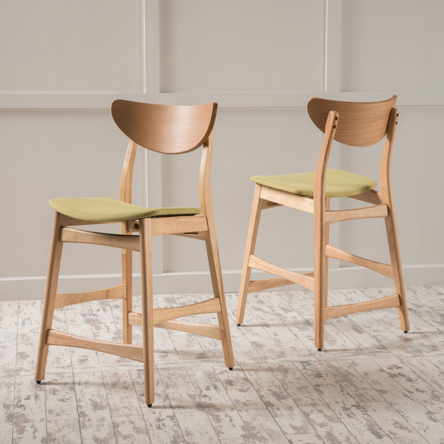 A set of Retro Modern Counter Height Chairs with cushioned seats in light green and curved backrests stands on a whitewashed wooden floor against a light paneled wall.