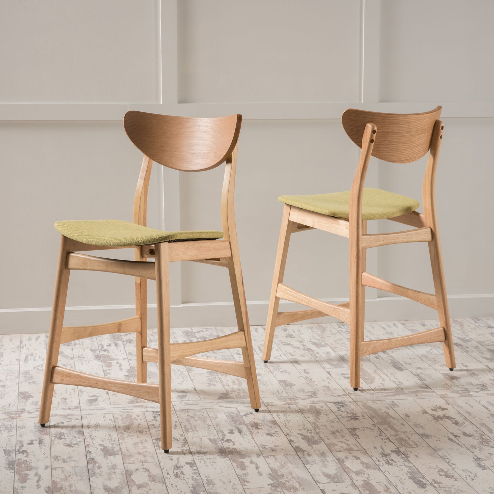 A set of Retro Modern Counter Height Chairs with cushioned seats in light green and curved backrests stands on a whitewashed wooden floor against a light paneled wall.