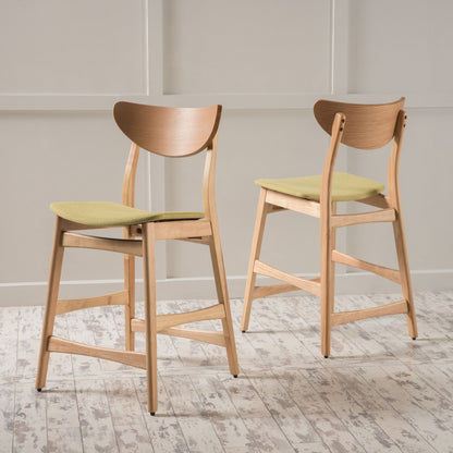 A set of Retro Modern Counter Height Chairs with cushioned seats in light green and curved backrests stands on a whitewashed wooden floor against a light paneled wall.