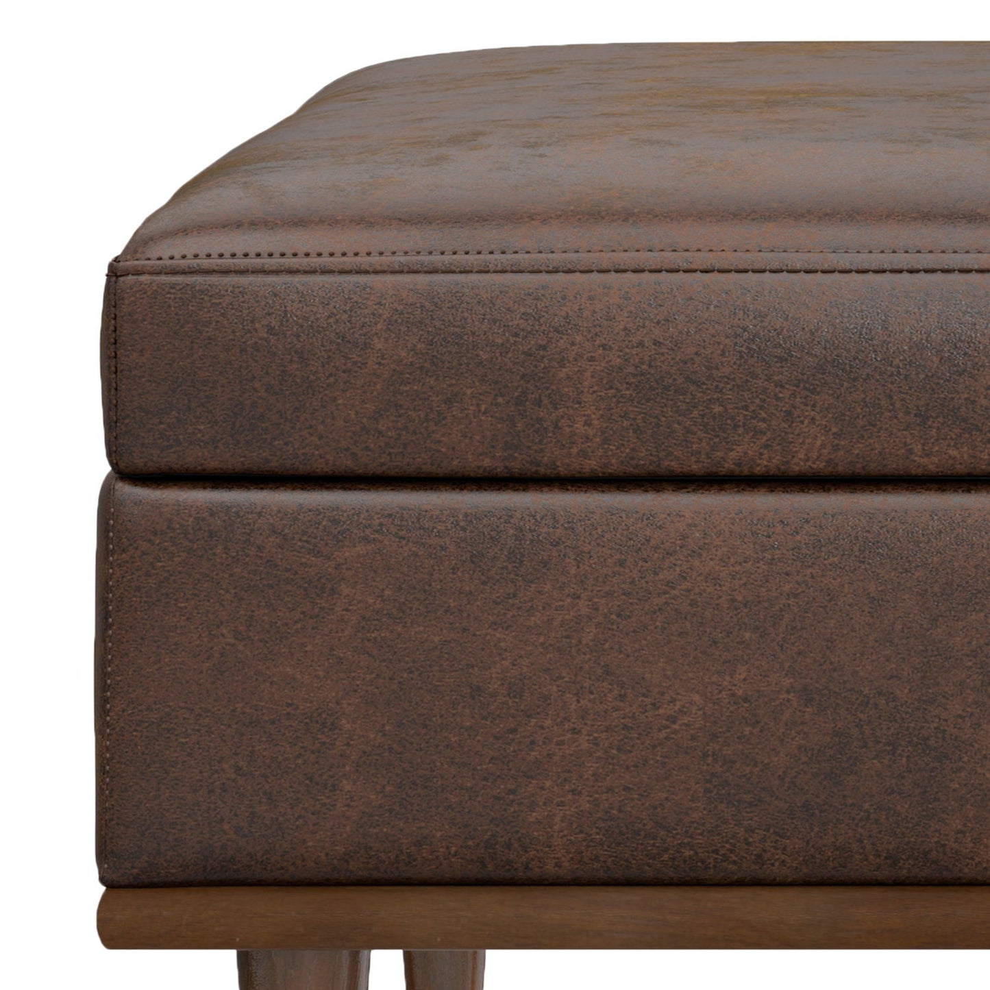Close-up of the Shiloh Multifunctional Square Storage Ottoman in brown faux leather, with visible stitching, a cushioned top, and partially visible wooden legs.