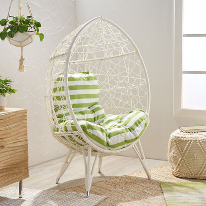 The Cosmos - Round Hammered Iron Teardrop Chair with green and white striped cushions sits in a bright room featuring textured walls, natural wood furniture, a woven pouf, a hanging plant, and sunlight streaming through the window.