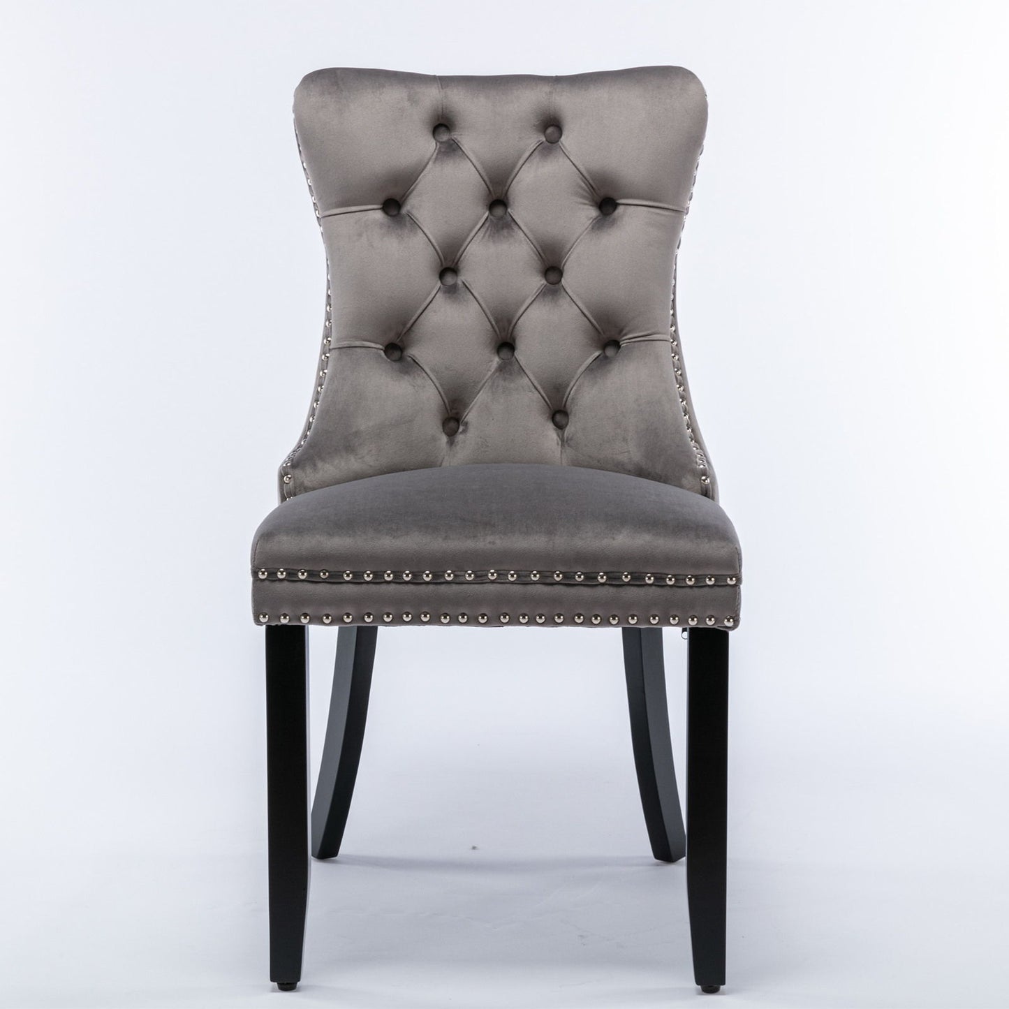 The Nikki chair set features modern, high-end velvet upholstery, a tufted backrest, silver nailhead trim, and dark wood legs—perfect for contemporary dining rooms.
