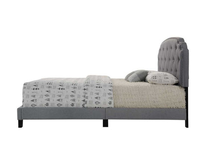 Side view of the Tradilla - Queen Bed in gray, featuring a modern tufted headboard, white bedding, patterned duvet, and two pillows. The neatly made bed is shown isolated on a white background.