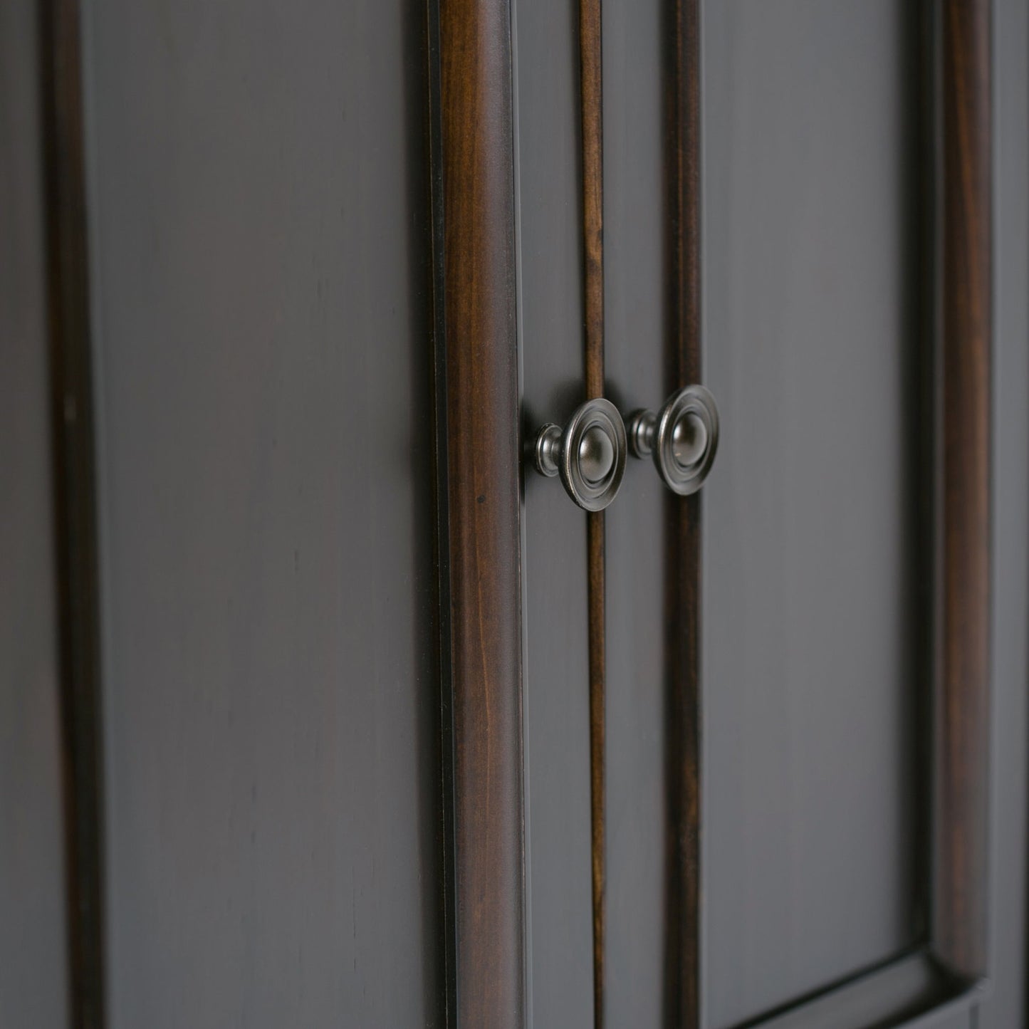 Close-up of the Amherst - Handcrafted Low Storage Cabinet, featuring dark smooth-finished wood, subtle grain, vertical trim accents, and two round silver handles centered on the doors.