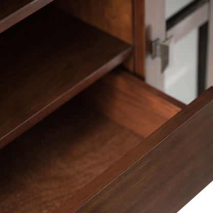 Close-up of an open wooden drawer and shelf with a dark brown finish on the Artisan - Handcrafted, Tall TV Media Stand, featuring a metallic handle and a glass panel on the right side.