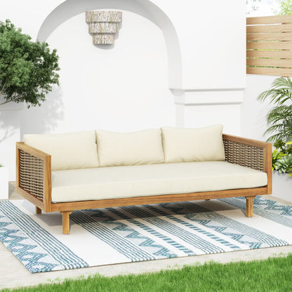 The Claremont 3 Seater Daybed Teak Acacia Wood with water-resistant cushions sits on a blue and white patterned rug in a bright patio, surrounded by green plants and white walls.
