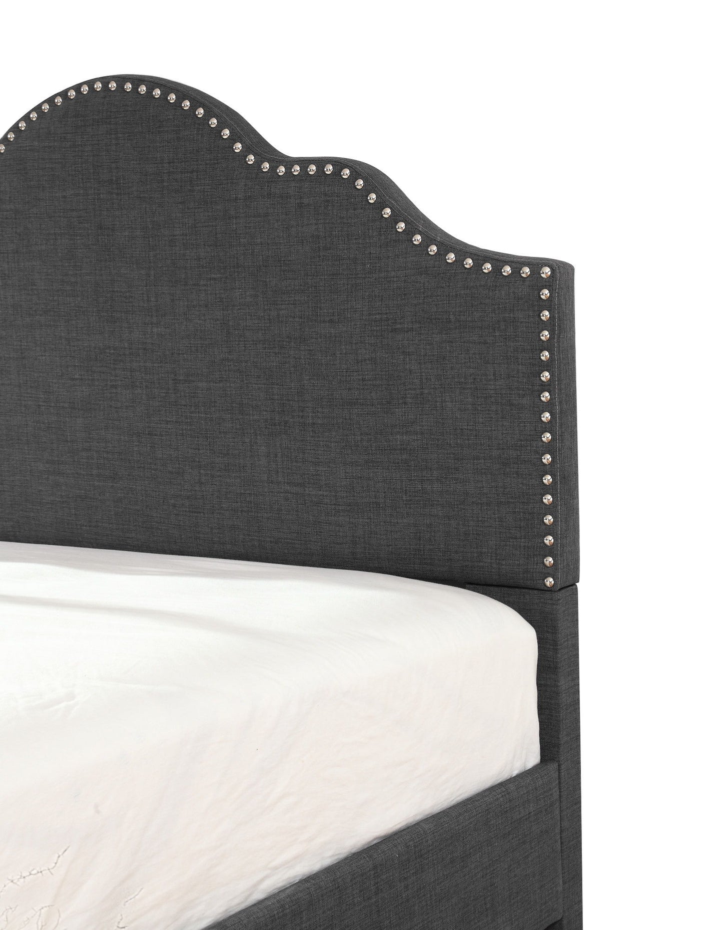 A close-up of the Kopa - Fabric Upholstered Bed in dark gray, featuring a curved headboard with silver nailhead trim along the edges. A white mattress is partially visible.