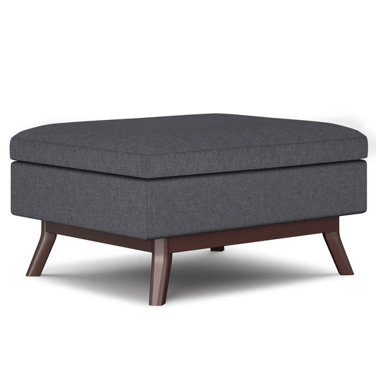 The Owen Upholstered Rectangular Storage Ottoman features a dark gray cushioned top and wooden legs, shown on a white background.