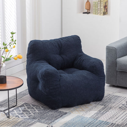 A Soft Teddy Fabric Tufted Foam Bean Bag Chair sits in a bright living room next to a small round table with a vase of yellow lemons, near a gray sofa and books on built-in shelves.
