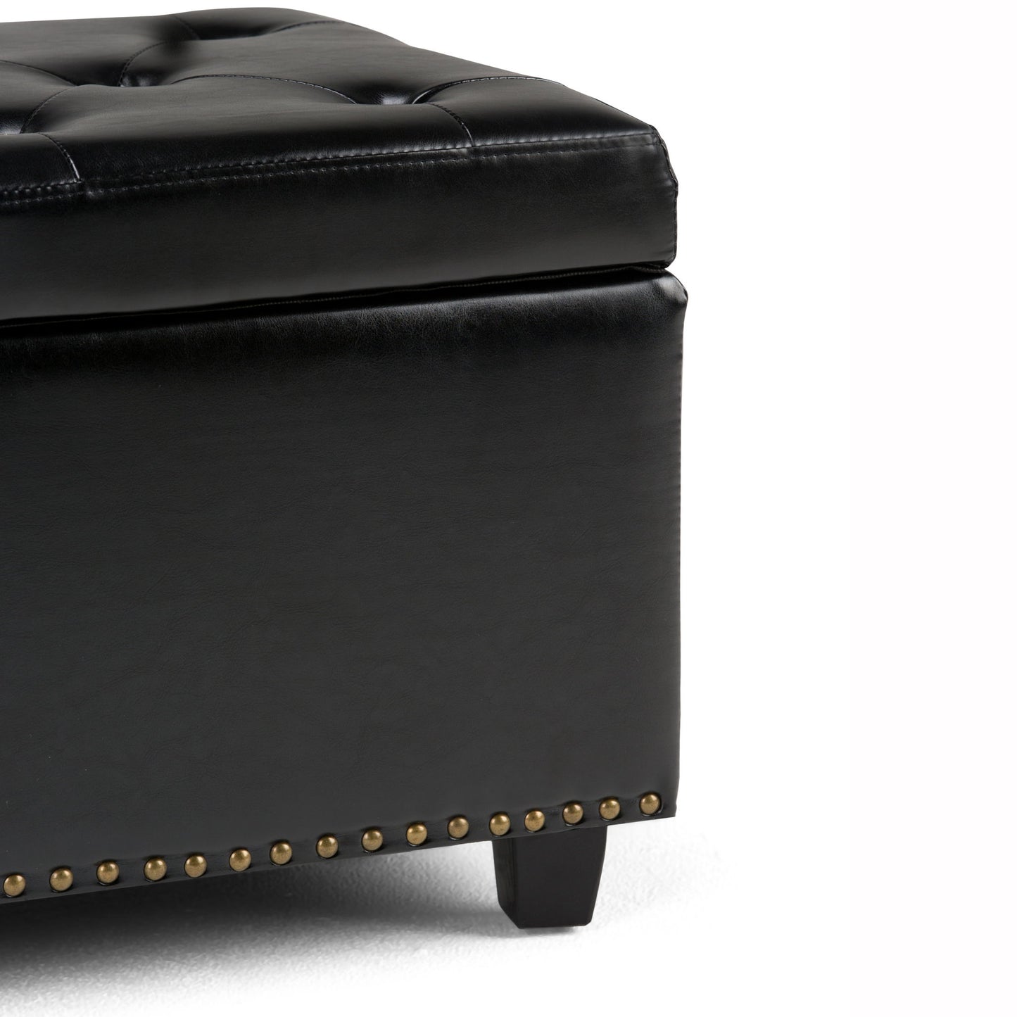 Close-up of the Hamilton Upholstered Storage Ottoman featuring a black tufted leather cushion, brass nailhead trim, and wooden legs on a white background.