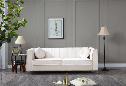 A modern living room featuring the Delray Micro Suede Sofa in beige, two round pillows, a gray wall, framed artwork, two lamps, a side table with books, a potted plant, and a gray rug with a decorative pillow and tray on the floor.