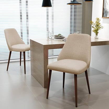 Two beige Modern Dining Chairs with iron legs and wood finish surround a modern light wood dining table set with plates, glasses, and a vase of yellow flowers. The table is placed near large windows with white blinds.