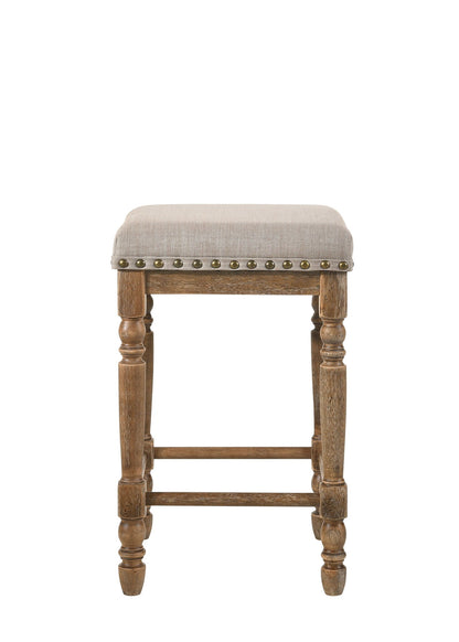 The Farsiris Weathered Counter Height Stool Set (2) in beige features turned wooden legs, a beige upholstered seat, and decorative metal studs along the edge, shown from the front against a white background.