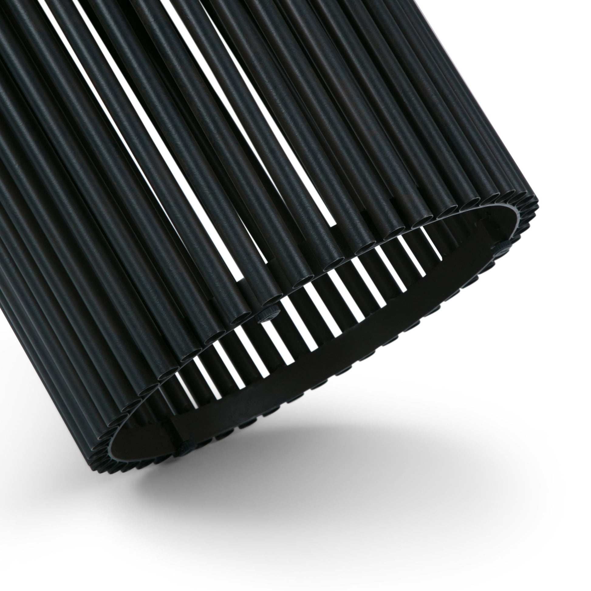 A close-up of the Demy Accent Table in natural and black, featuring a cylindrical design with evenly spaced vertical slats. Light passes through the gaps, creating a striking striped effect against a white background.