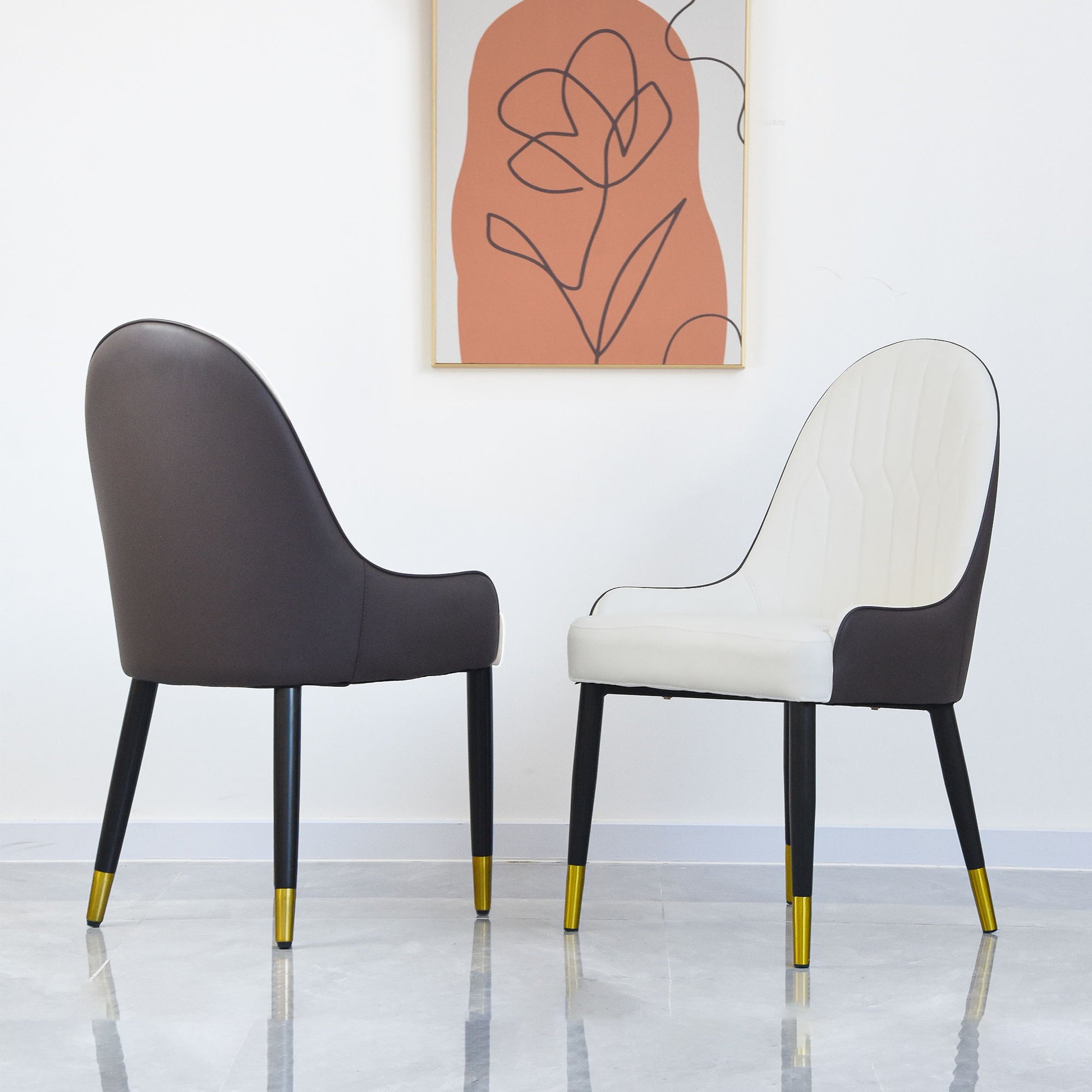 A set of two Modern PU Sponge-Filled Dining Chairs with solid wood and metal legs—one white, one dark grey—stand on a light floor beneath a minimalist framed abstract art piece on a white wall.