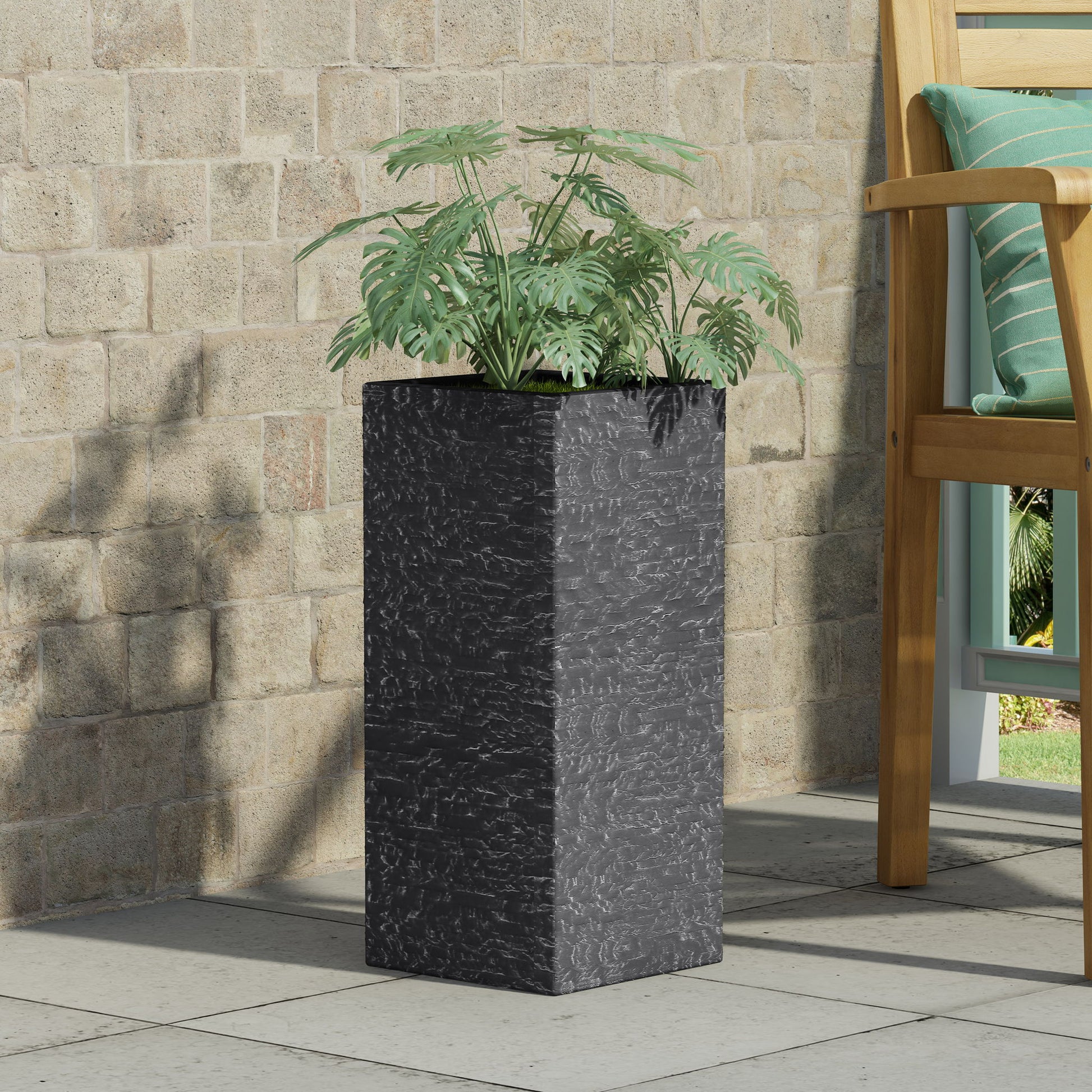 A Modern Outdoor Planter with leafy green plants sits on a tiled patio near a brick wall and a wooden chair with a green cushion.