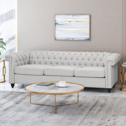 A modern living room with a Chesterfield Style 3 Seater Sofa With Deep Button Tufting in light gray, a round marble coffee table with gold legs, cup and saucer, side tables, abstract art on a beige wall, and a light gray rug.