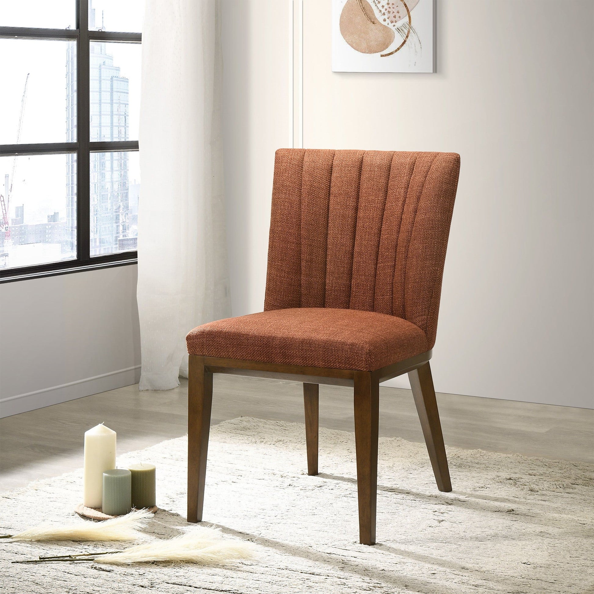 The Elmwood - Stylish Dining Chair (Set of 2) features rust-colored upholstery and wooden legs, set on a light rug in a bright room with large windows, candles, and abstract wall art.