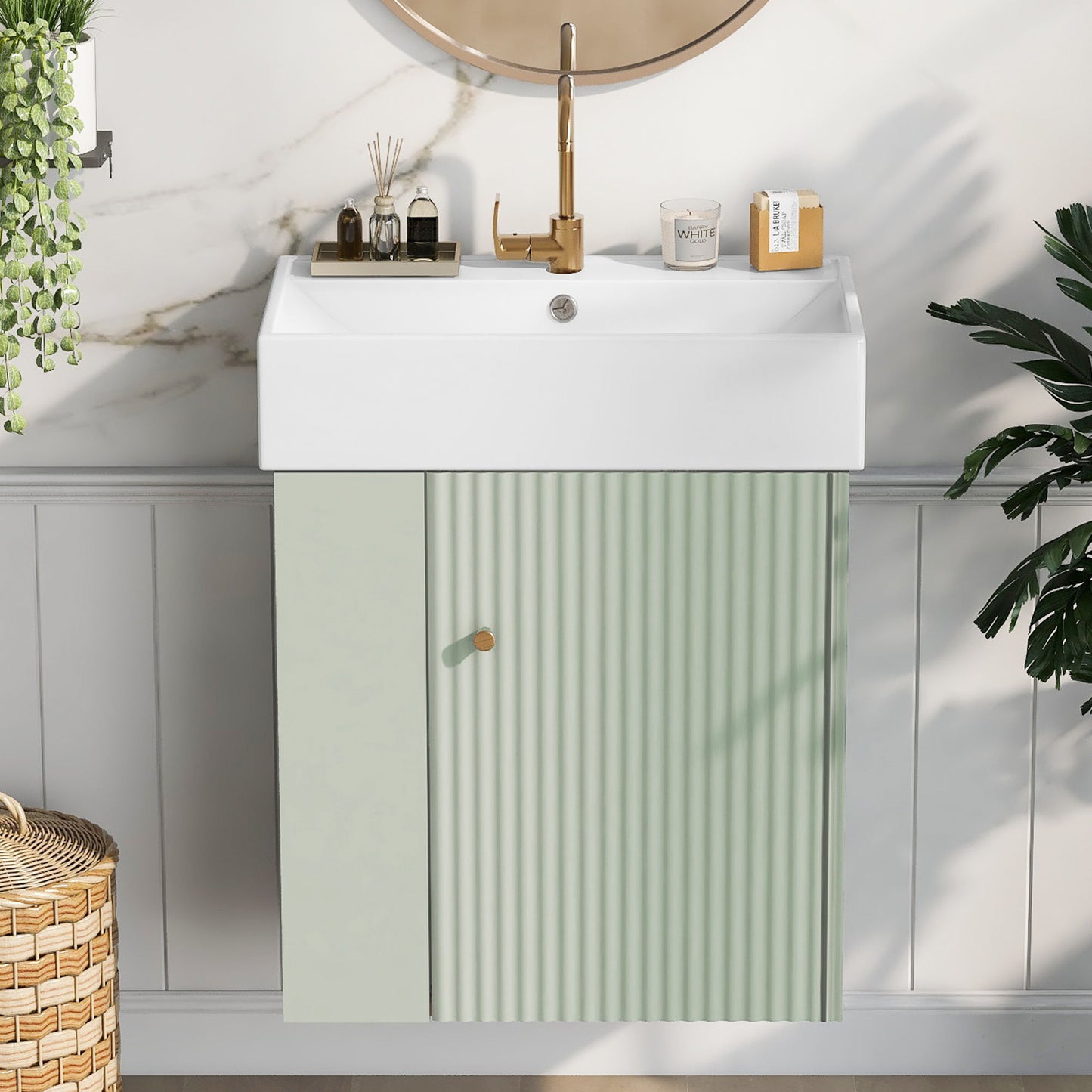 The Modern Floating Bathroom Vanity With Ceramic Basin is paired with a gold faucet and sits beneath a round mirror. Vertical grooves detail the pale green unit, while decor, plants, and a wicker basket complete the stylish small bathroom look.