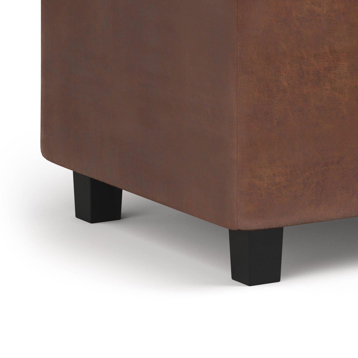 Close-up of the corner of the Cosmopolitan Upholstered Storage Ottoman in brown leather, featuring two black wooden legs, set against a white background.