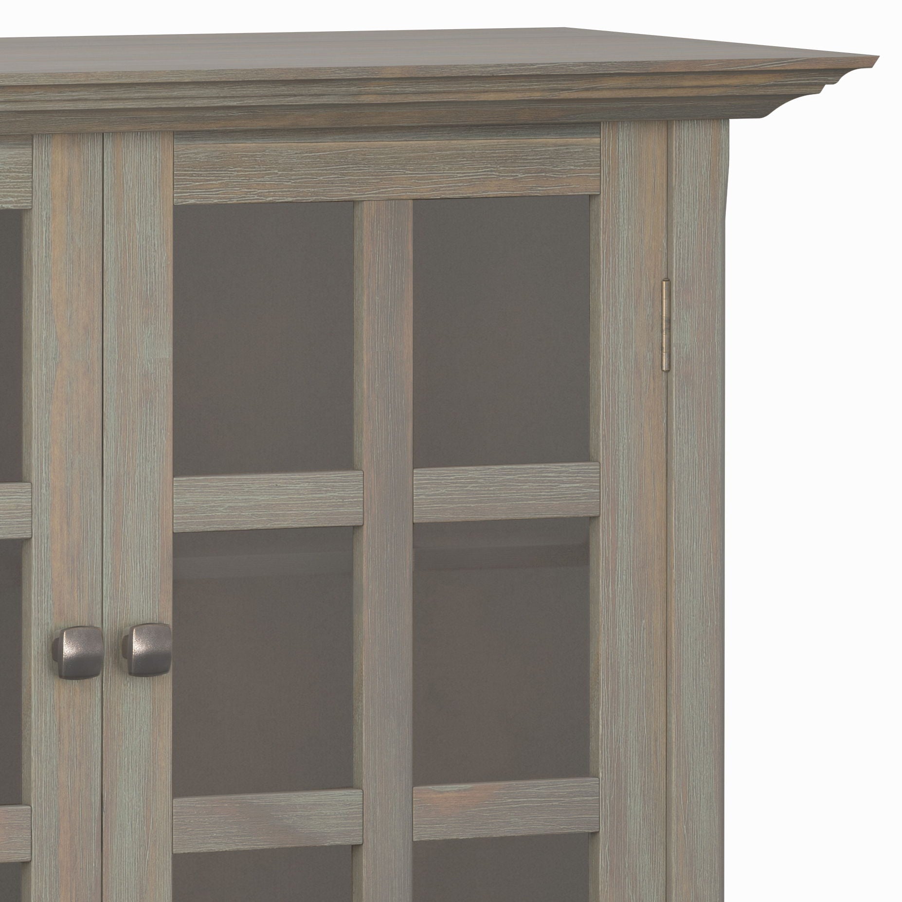 Partial view of the Acadian - Medium Storage Cabinet, Handcrafted, featuring glass-paneled doors with two square handles, a decorative top edge, and a light, weathered wood finish.