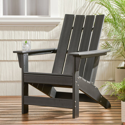 An Enigmara Outdoor High Density Resin Adirondack Chair in black sits on a wooden deck by a white wall with a window, holding a glass of drink on its armrest. Potted green plants are placed nearby for a fresh touch.