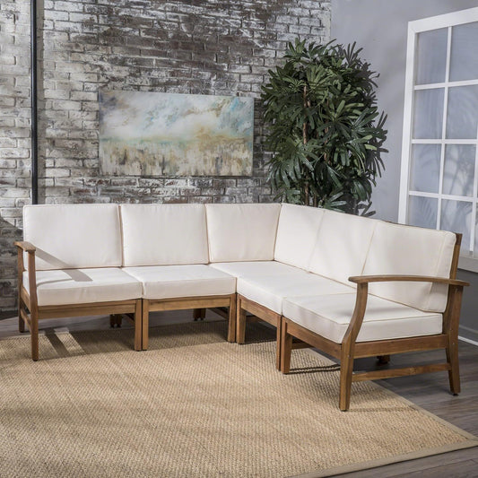 The Perla - 5 Pieces Sofa Set with white cushions is arranged on a woven rug in a room featuring a gray brick wall, abstract art, a large potted plant, and a window with white trim.