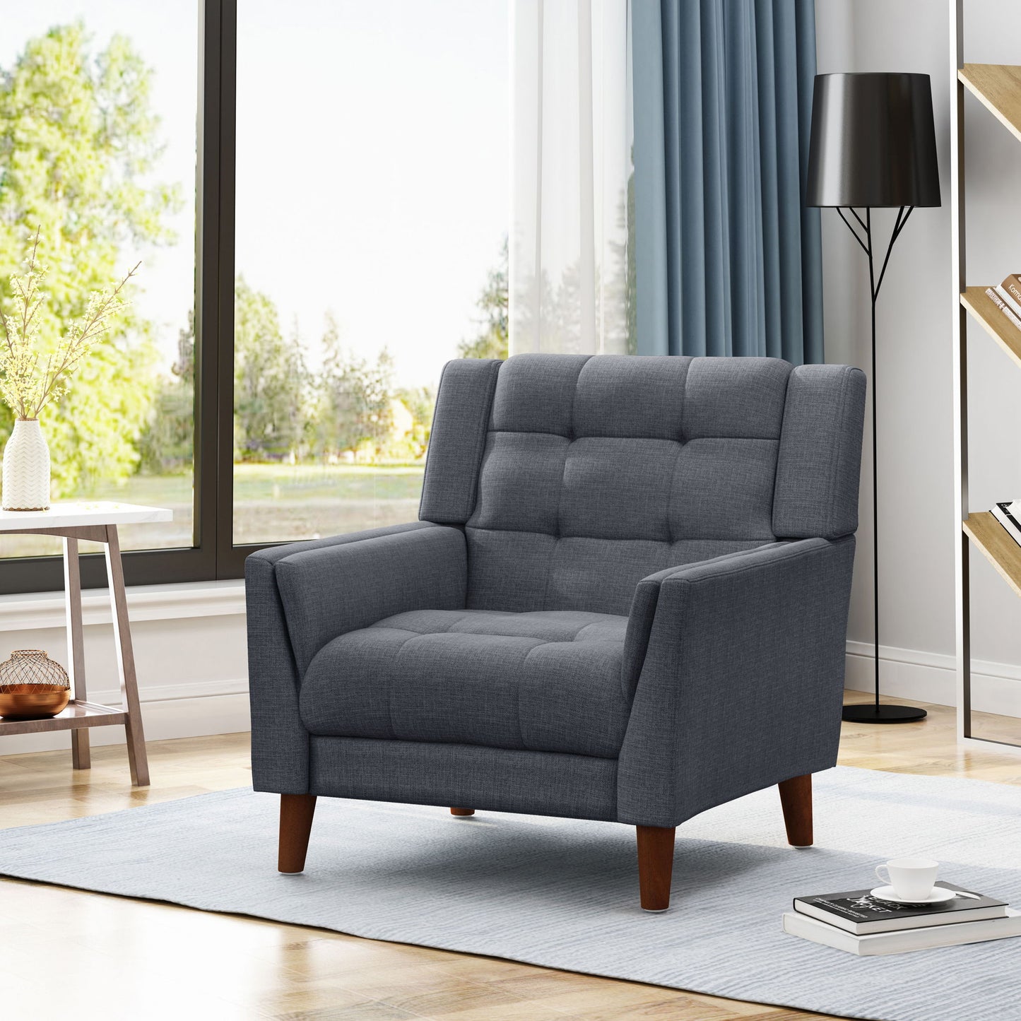 The Luminaesque - Fabric Upholstered Armchair With Tufted Back, in modern gray with wooden legs, is placed on a light blue rug in a bright living room featuring large windows, a black floor lamp, and a bookshelf.