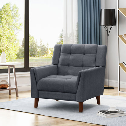 The Luminaesque - Fabric Upholstered Armchair With Tufted Back, in modern gray with wooden legs, is placed on a light blue rug in a bright living room featuring large windows, a black floor lamp, and a bookshelf.