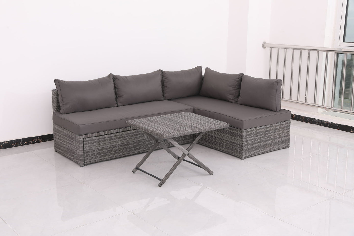 The Patio Sofa With Cushions - Gray and a matching rattan-style coffee table are placed on a white tiled floor in a bright, minimalist room with white walls and a metal railing.