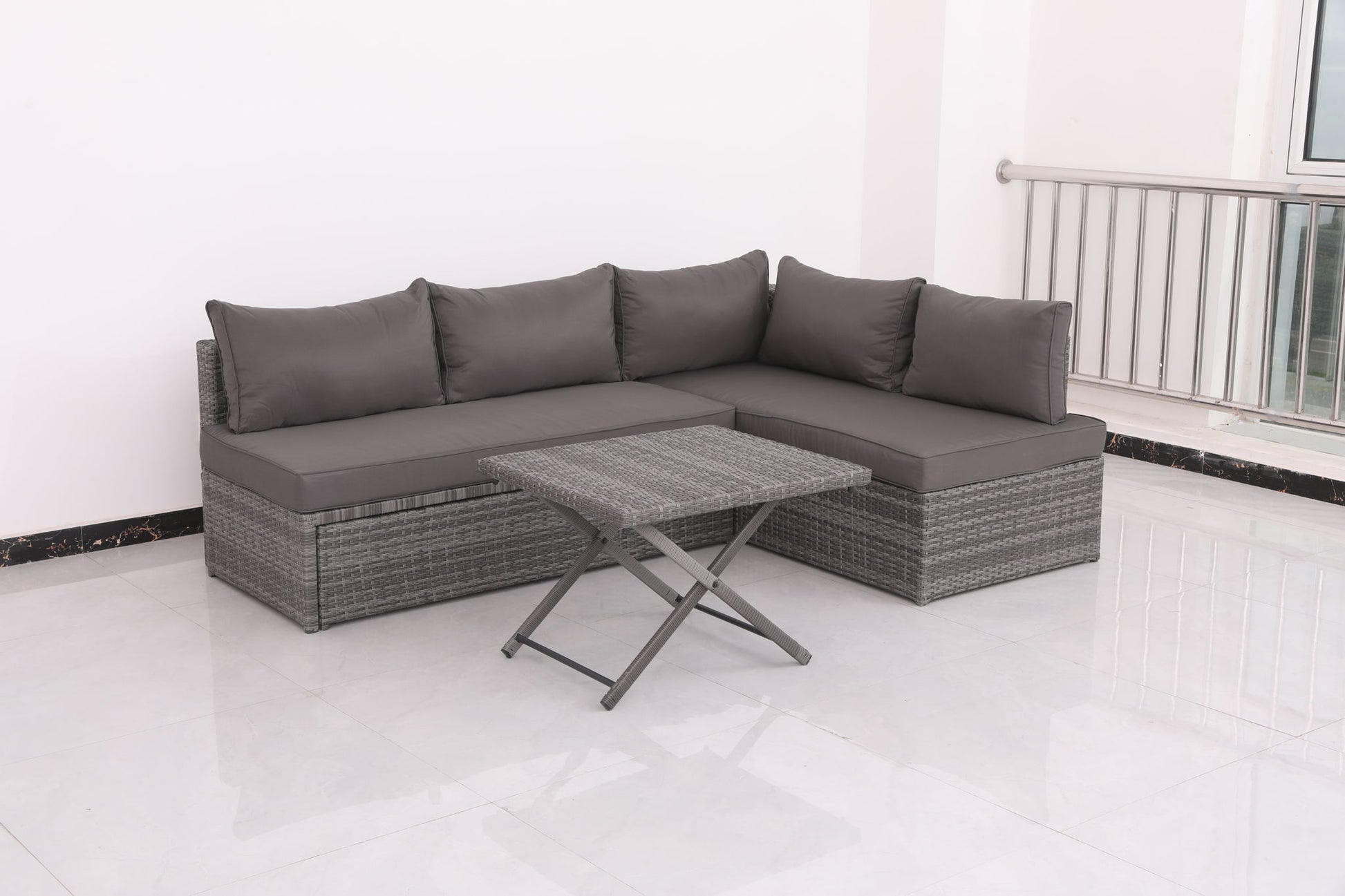 The Patio Sofa With Cushions - Gray and a matching rattan-style coffee table are placed on a white tiled floor in a bright, minimalist room with white walls and a metal railing.