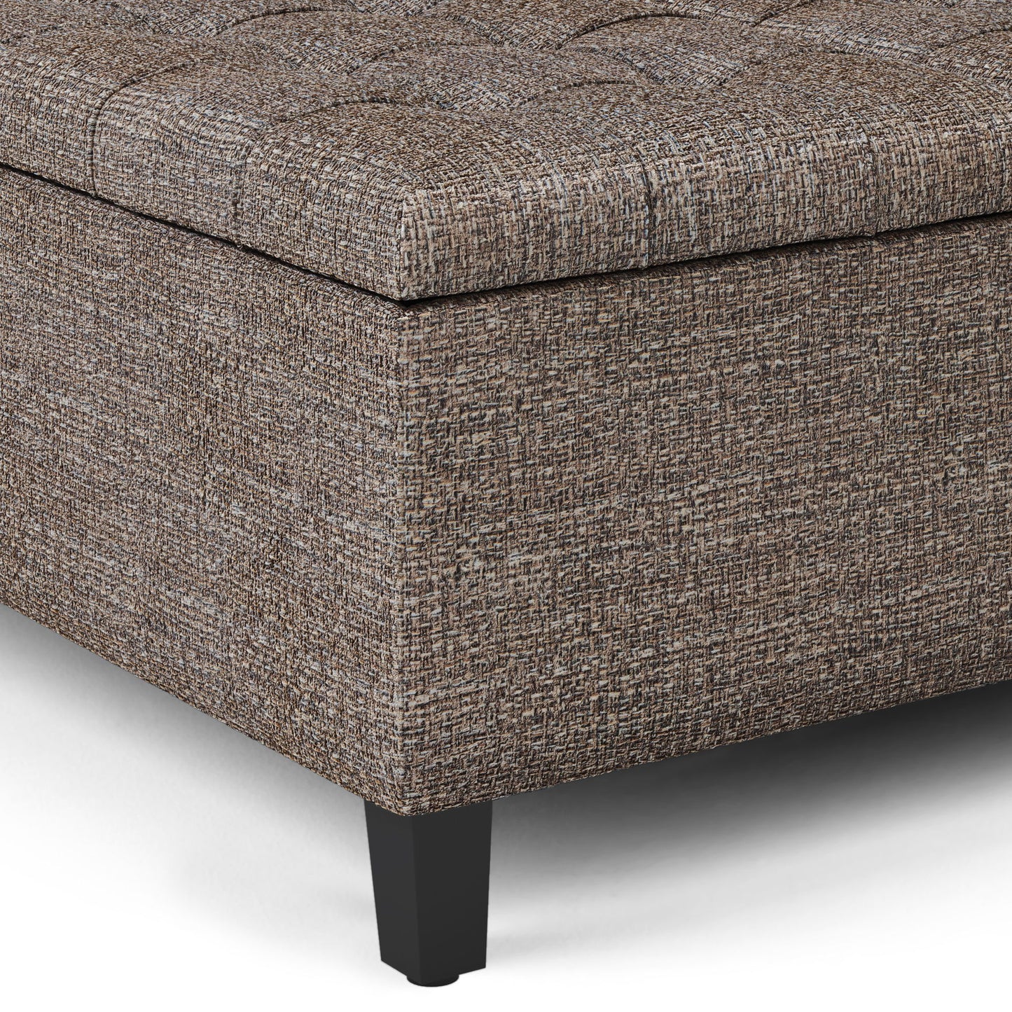 Close-up of the Harrison Upholstered Coffee Table Storage Ottoman corner, featuring textured brown and gray fabric, a tufted top, and black tapered legs on a white background.