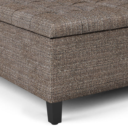 Close-up of the Harrison Upholstered Coffee Table Storage Ottoman corner, featuring textured brown and gray fabric, a tufted top, and black tapered legs on a white background.