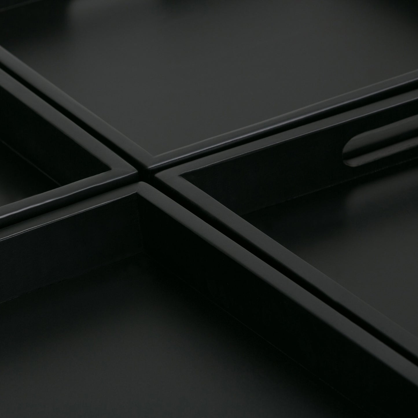 Close-up of Avalon - Square Coffee Table, Storage Ottoman: intersecting black rectangular trays with raised edges form a geometric grid. An oval cut-out handle and smooth, sharp lines add to the table's minimalist, modern aesthetic.