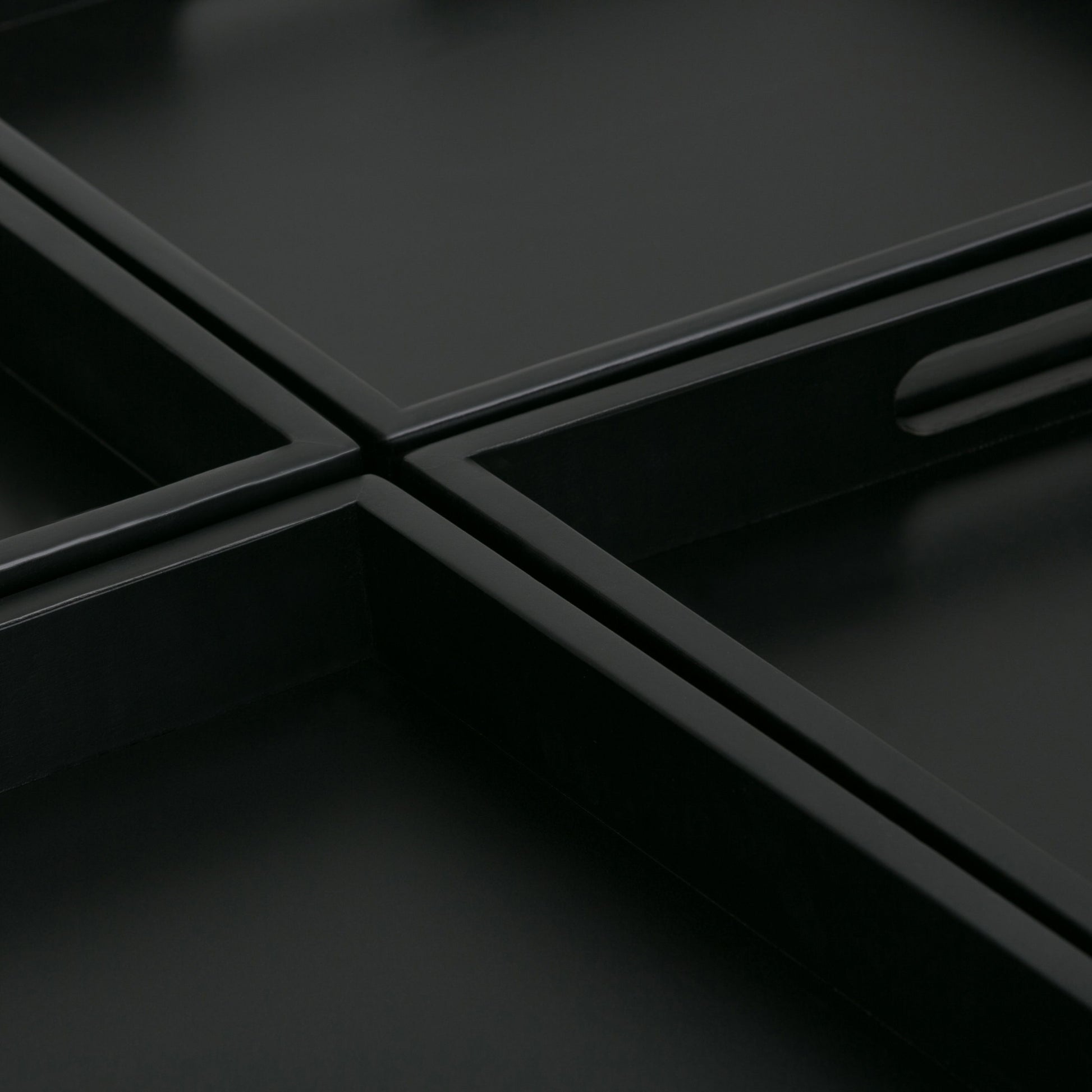 Close-up of Avalon - Square Coffee Table, Storage Ottoman: intersecting black rectangular trays with raised edges form a geometric grid. An oval cut-out handle and smooth, sharp lines add to the table's minimalist, modern aesthetic.