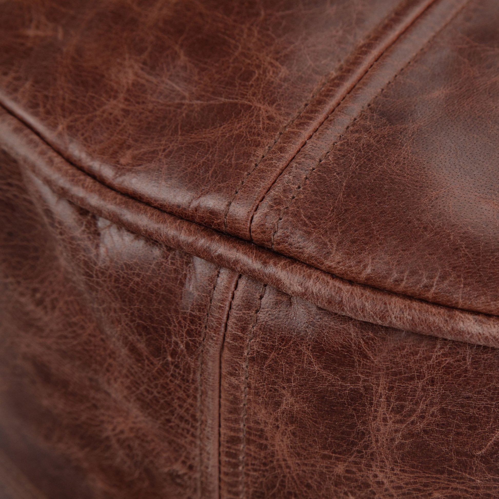 Close-up of the Connor Handcrafted Round Pouf’s brown, textured leather upholstery featuring visible stitching and natural creases.