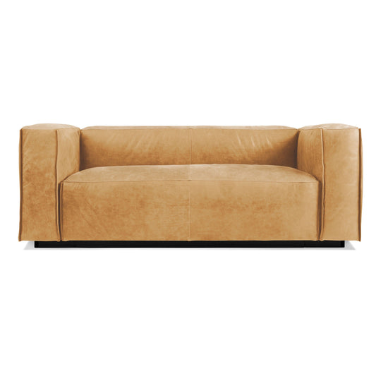 The Cleon Leather Armed Sofa in Camel Leather features a modern, boxy silhouette with broad armrests and a low backrest. Its minimalist, contemporary design includes smooth, clean lines and is displayed against a white background.