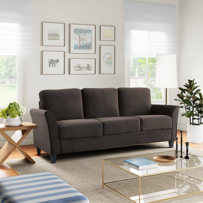 A modern living room features the Lifestyle Solutions Wesley 80.3 in. dark grey sofa, a wooden side table with plants, glass coffee table with books, striped ottoman, floor lamp, framed wall art, and large windows bringing in natural light.