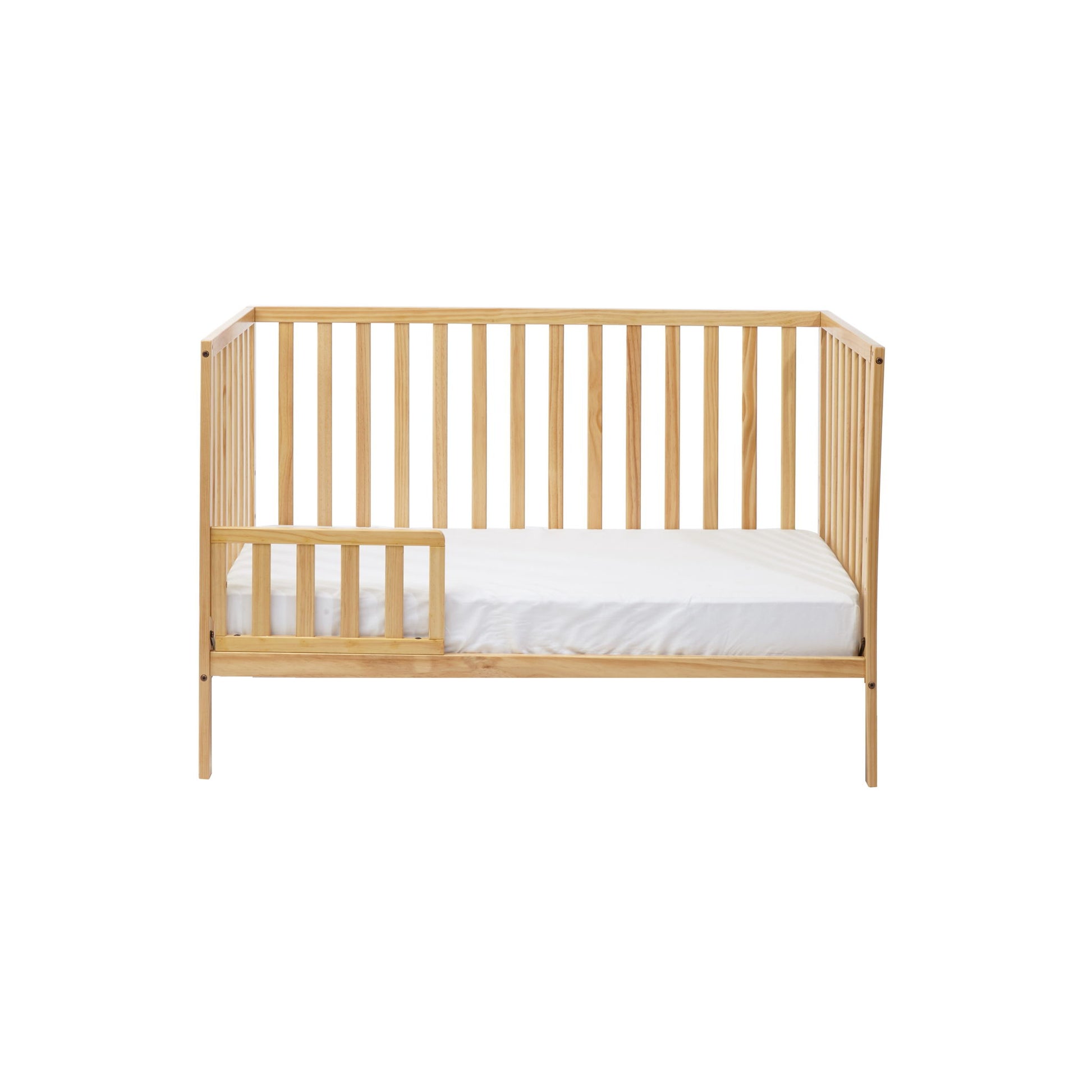 The Palmer - 3-in-1 Convertible Island Crib features a light wood finish, vertical slats on all sides, an open space with a small guard rail on one side, and comes with a white mattress inside.