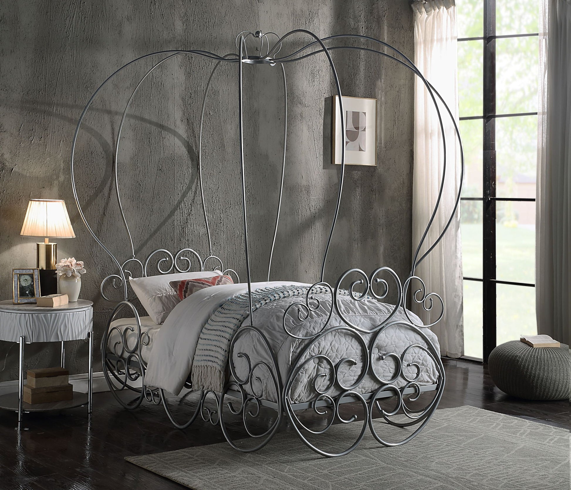 A whimsical bedroom featuring the Priya Twin Bed With Canopy in silver, ornate metal scrollwork, a gray comforter, a side table with a lamp, and large windows letting in natural light.