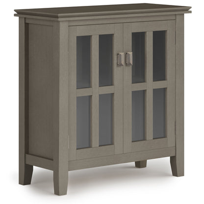 Artisan - Handcrafted Low Storage Cabinet features a gray wooden build, glass-paneled double doors with metal handles, a rectangular top, four short legs, and a simple modern design.