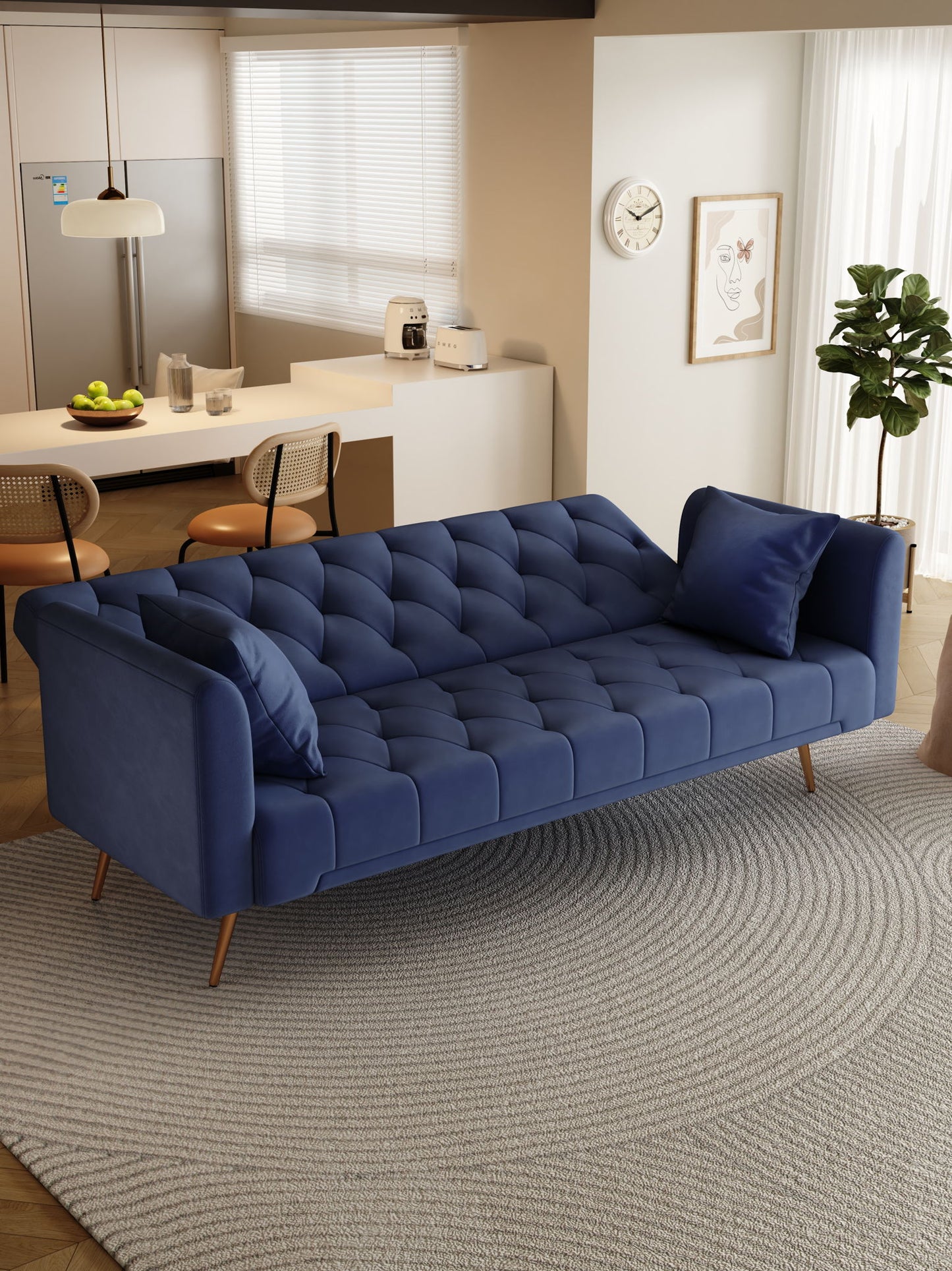 A modern living room with a Convertible Double Folding Living Room Sofa Bed in blue, matching pillows, a round gray rug, potted plant, wall clock; in the background: kitchen with bar stools, fridge, and fruit on the counter.