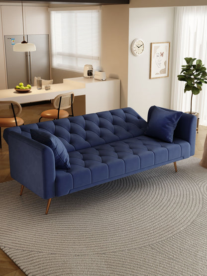 A modern living room with a Convertible Double Folding Living Room Sofa Bed in blue, matching pillows, a round gray rug, potted plant, wall clock; in the background: kitchen with bar stools, fridge, and fruit on the counter.