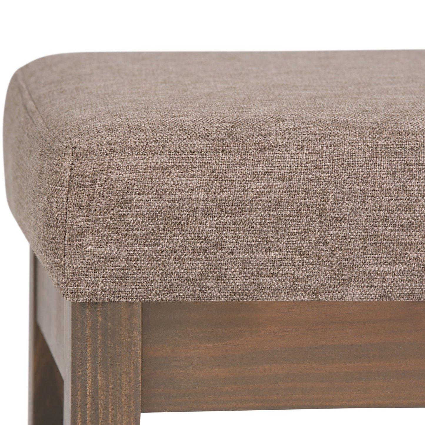 Close-up of the Milltown - Upholstered Ottoman Bench, highlighting its light brown textured fabric seat and wooden legs at the corner and side.