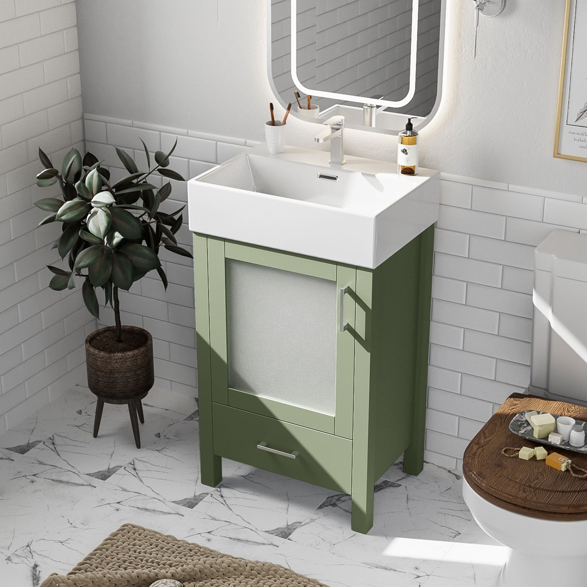 A small bathroom features a Bathroom Vanity With Ceramic Sink And Ample Storage, ideal for small spaces, paired with a rectangular mirror, potted plant, white tiled walls, marble floor, and a toilet with wooden seat. Toiletries are neatly arranged.