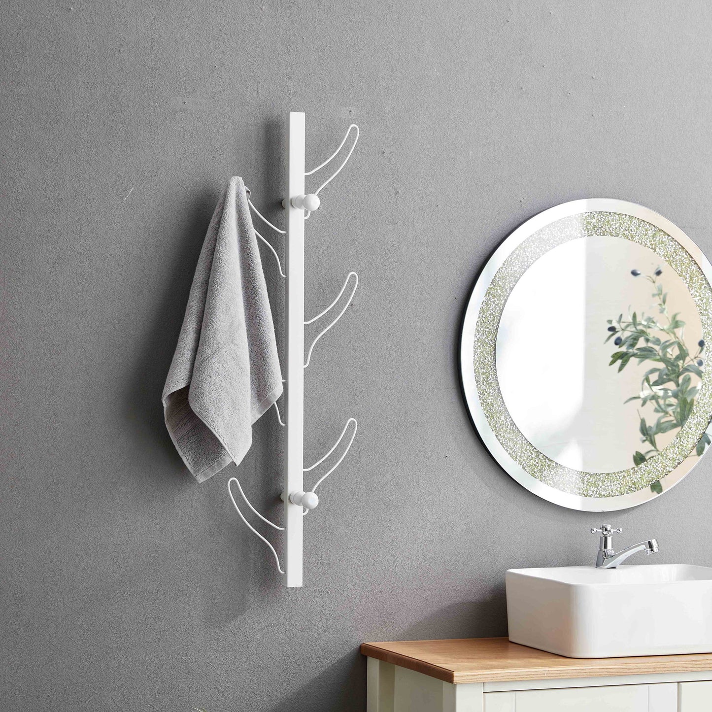 A gray towel hangs on the Vertical Eight Hook Coat Rack Wall Mount beside a round mirror above a white sink and light wood vanity in a bathroom with gray walls.