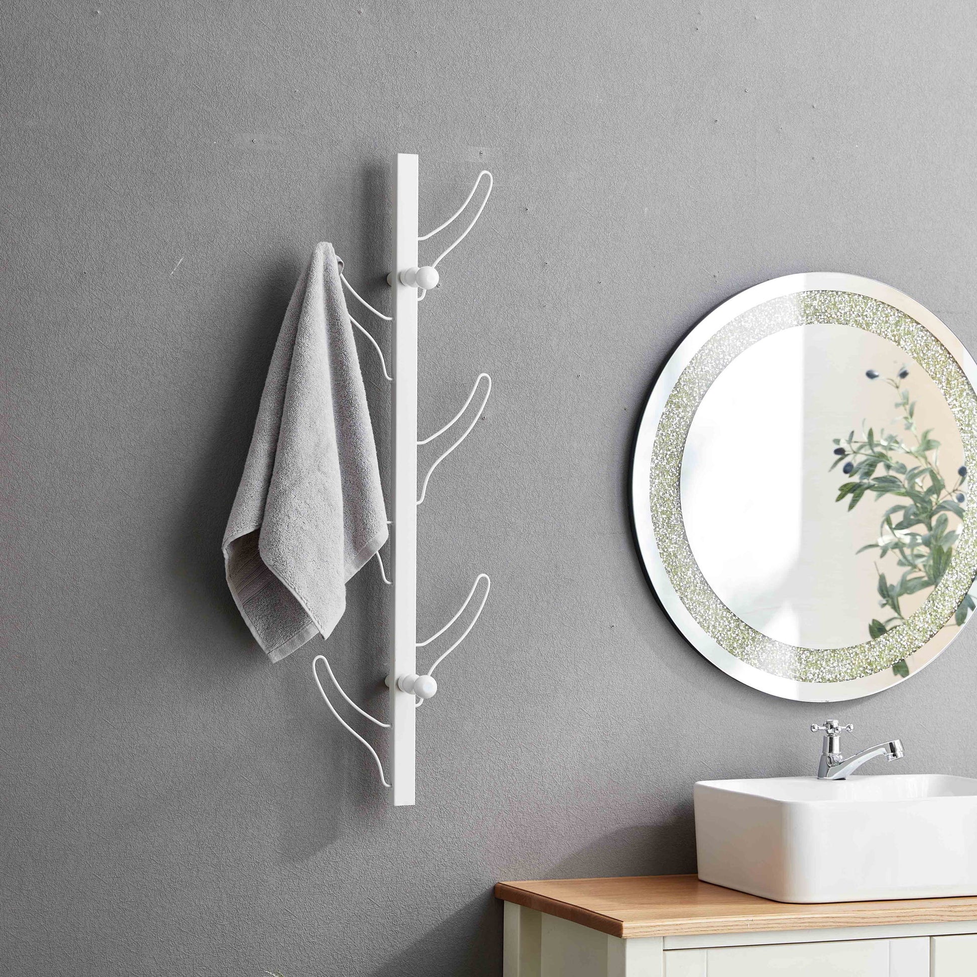 A gray towel hangs on the Vertical Eight Hook Coat Rack Wall Mount beside a round mirror above a white sink and light wood vanity in a bathroom with gray walls.