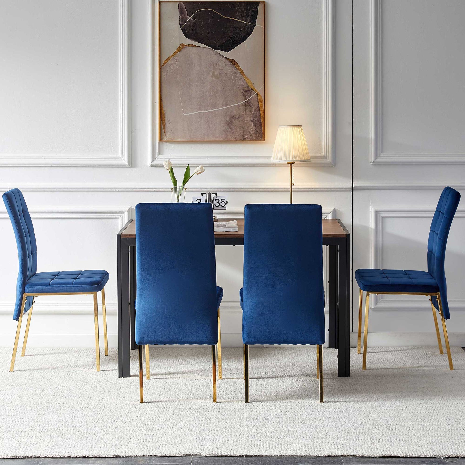 A modern dining room featuring the 5 Pieces Dining Set with a creative design table and four velvet high back chairs with golden legs, paired with a lamp, white flower vase, and abstract wall art on a white paneled wall.