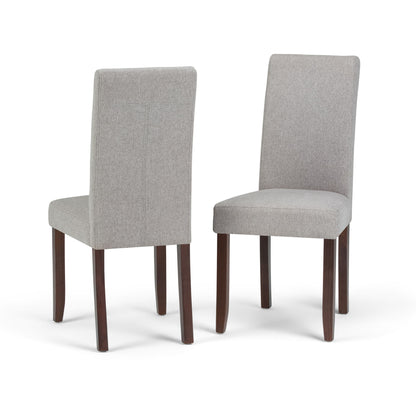 The Acadian Upholstered Parson Dining Chair set includes two chairs with light gray fabric seats and backs, dark wooden legs, and is shown against a white background—one chair facing front, the other displaying the back.